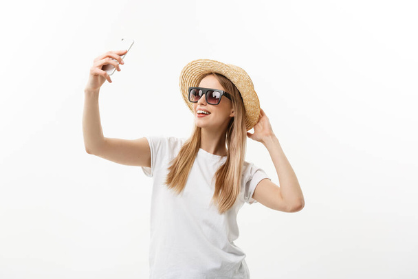 Mode et Lifestyle Concept : jolie jeune femme portant un chapeau, lunettes de soleil prenant une photo d'elle-même par téléphone portable isolé sur fond blanc - Photo, image