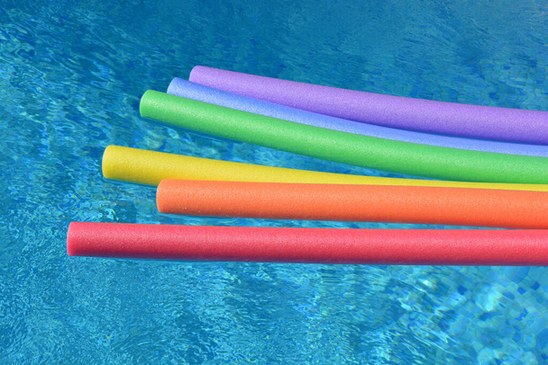 Fideos de color arco iris flotando en una piscina en un día soleado y luminoso. Divertido ambiente de vacaciones de verano
. - Foto, Imagen