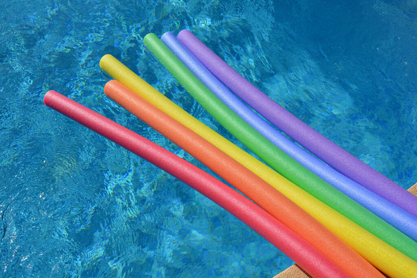明るく晴れた日にスイミングプールに浮かぶ虹色のプール麺、楽しい夏の休日の振動 - 写真・画像