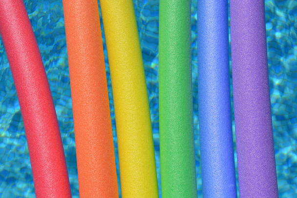 Regenboog gekleurde zwembad noedels drijven in een zwembad. Leuke zomerse vibes - Foto, afbeelding