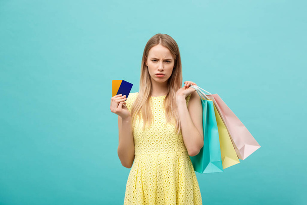 Portrait of a sad woman holding shopping bags and bank card isolated on a blue background - Foto, Bild