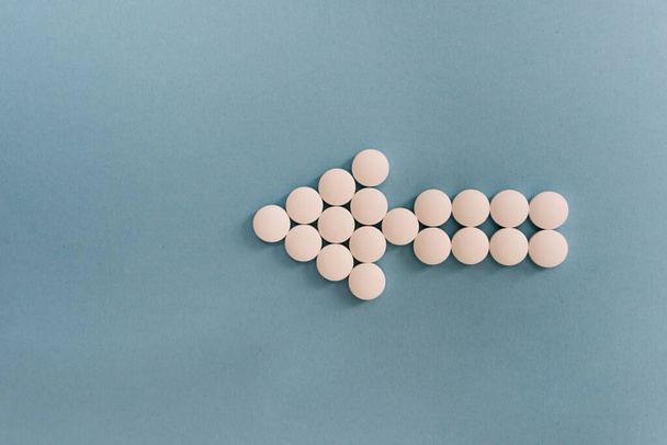 Stock photo of a bunch of different pills placed on a blue background in the shape of an arrow. There is nobody on the picture. - Фото, изображение