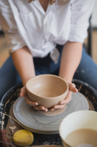 The female potter finished making a clay vase remove it from the potters wheel. Creating vase of white clay. Making ceramic products from white clay, closeup - Photo, Image