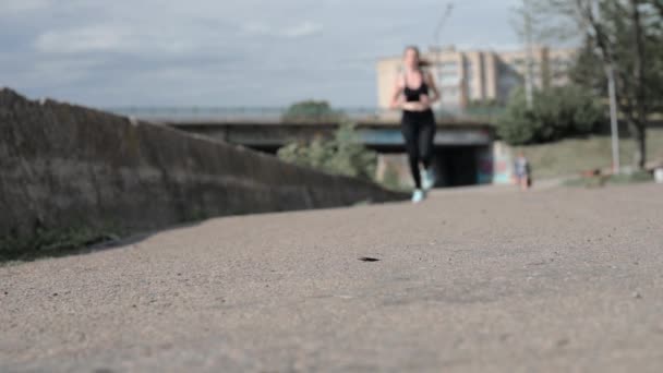 Młoda kobieta wiąże sznurowadła podczas joggingu. Zbliżenie dopasowanej kobiety wiąże sznurowadła stojąc na asfaltowej drodze. Niewyraźne działanie. - Materiał filmowy, wideo