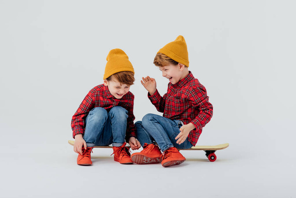 Glad twin brothers sitting on skateboards and laughing - 写真・画像