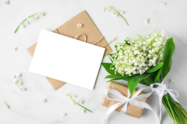 чиста вітальна листівка з ліліями букета квітів долини та подарункова коробка на білому тлі. знущатися. вид зверху. плоска лежала. запрошення на весілля
 - Фото, зображення