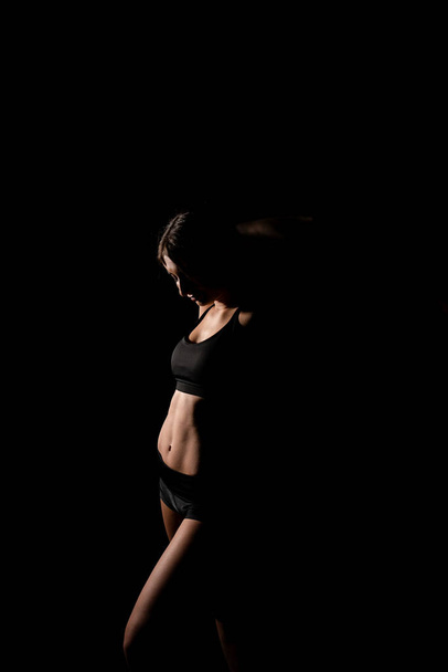 Close up girl shows sports stomach. Healthy fitness and eating lifestyle concept. Fitness sporty woman showing her well trained body, isolated over black background. - Φωτογραφία, εικόνα