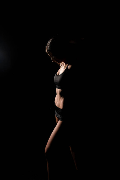 Close up girl shows sports stomach. Healthy fitness and eating lifestyle concept. Fitness sporty woman showing her well trained body, isolated over black background. - Foto, Imagem