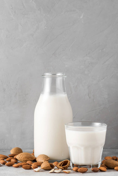 Amandelmelk in een fles met glas en amandelnoten op een betonnen ondergrond. Veganistische zuivel vrije plantaardige melk. verticale oriëntatie. close-up - Foto, afbeelding