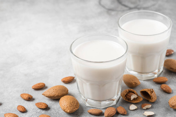 Plantaardige amandel veganistische melk in glazen met noten op betonnen achtergrond. Zuivelvrije melk. close-up - Foto, afbeelding
