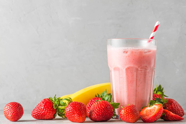 Φράουλα και smoothie μπανάνα ή milkshake σε ένα ποτήρι με καλαμάκι με φρέσκα φρούτα. δροσιστικό καλοκαιρινό ποτό. Κλείσιμο - Φωτογραφία, εικόνα