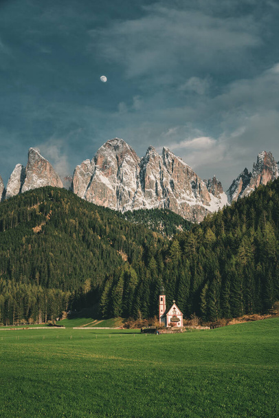 Piękny widok kościoła św Jana w Ranui w włoskiej miejscowości Santa Maddalena w Dolomitach Alpy o zachodzie słońca. Val di Funes, Południowy Tyrol, Włochy, Europa. Orientacja pionowa - Zdjęcie, obraz