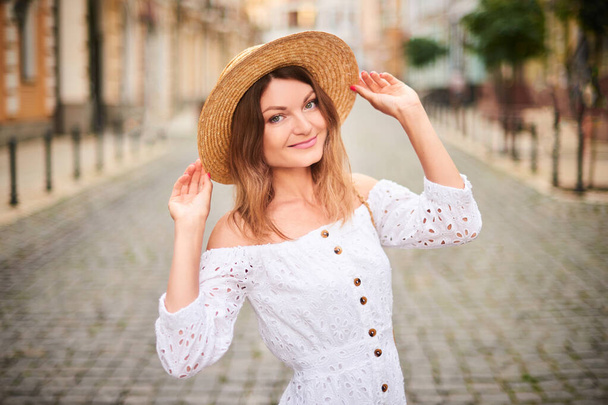 mosolygós lány sétál az utcán az óváros közepén. nő szalma kalap a nyári utazás - Fotó, kép
