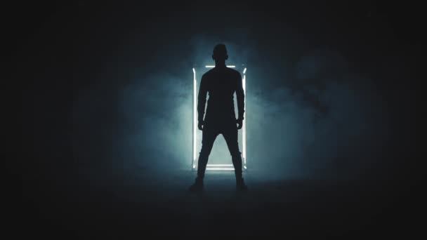 Silhouette di giovane uomo in piedi nella stanza fumosa scura con luce bianca - Filmati, video