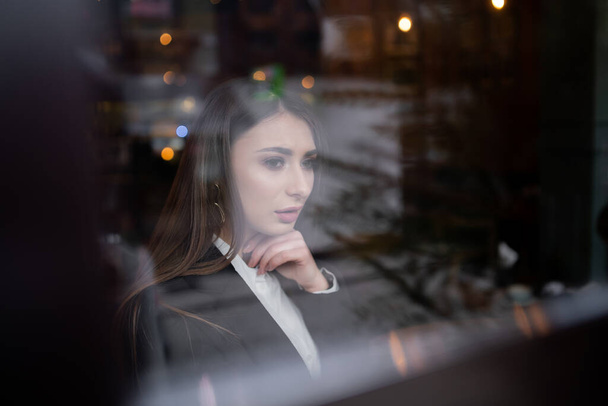 Camın arkasındaki güzel esmer kız, pencerede genç bir kadının portresi, kadın duyguları konsepti. Pencereden bakan bir kadın model. Dikey - Fotoğraf, Görsel