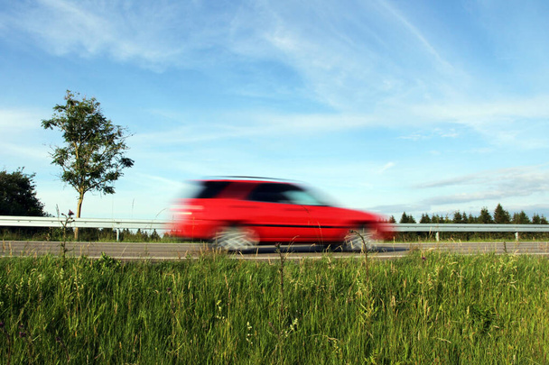 Ένα κόκκινο αυτοκίνητο οδηγεί πολύ γρήγορα πάνω από ένα δρόμο - Φωτογραφία, εικόνα