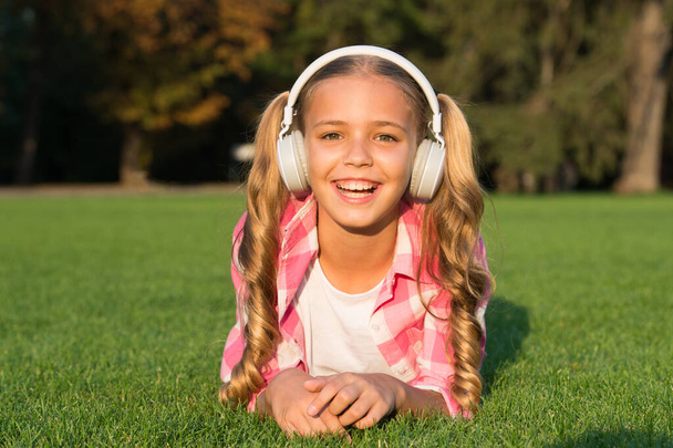 ascoltare musica. Torniamo a scuola. studio dei bambini nel parco. rilassarsi sull'erba verde in cuffia. piccola ragazza ascoltare audiolibro. nuova tecnologia per i bambini. ricordi d'infanzia felici. Imparare oggi. - Foto, immagini