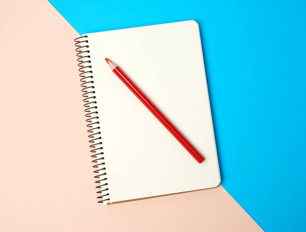 lápis de madeira vermelho e caderno aberto em espiral com folhas brancas em branco em um fundo azul, vista superior
 - Foto, Imagem