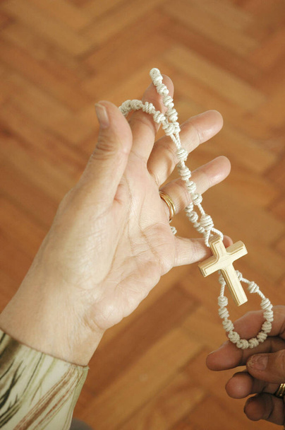 Handen van volwassen vrouw bidden met een rozenkrans - Foto, afbeelding