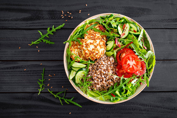 Lunch bowl with buckwheat porridge, fried chicken cutlets and fresh vegetable salad of arugula, lettuce, chard leaves, tomato, cucumber and flax seeds - Foto, imagen