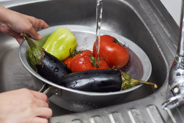 Mulher lavando legumes orgânicos recém-colhidos em escorredor antes de preparar salada saudável
 - Foto, Imagem