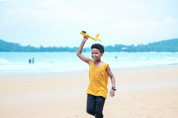 Cute kid boy having fun on sandy summer beach with blue sea, happy childhood boy playing model plane on tropical beach - Photo, Image