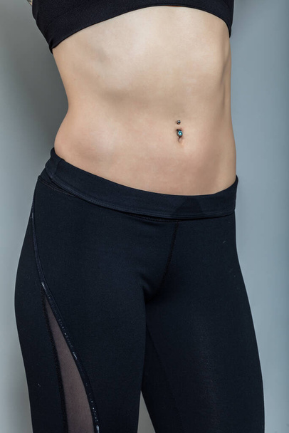 close-up of a sporty female belly with a pierced navel on a gray background. - Zdjęcie, obraz