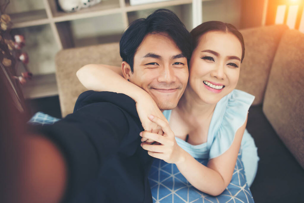 Šťastný pár se směje a bere selfie s telefonem sedí na gauči doma - Fotografie, Obrázek