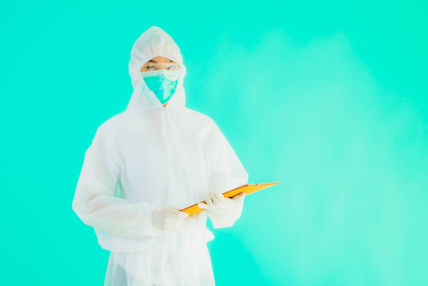 Portrait beautiful young asian doctor woman wear ppe or  personal protective equipment for protect from coronavirus or covid19 with empty card white board on blue isolated background - Photo, Image