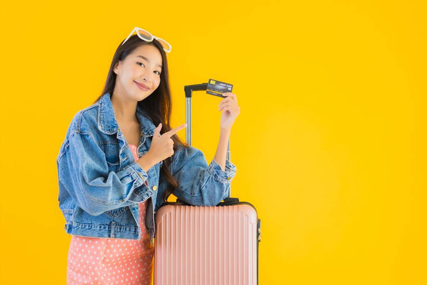 パスポート付きの荷物旅行バッグと黄色の隔離された背景に搭乗券を持つ肖像画の美しい若いアジアの女性 - 写真・画像