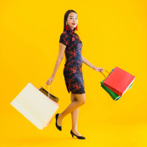 Retrato bela jovem asiática usar vestido chinês com saco de compras, telefone celular inteligente, cartão de crédito para o ano novo chinês no fundo isolado amarelo
 - Foto, Imagem