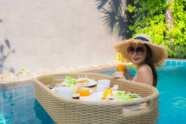 ポートレート若いアジアの女性幸せな笑顔は、ホテルのリゾートでプールで浮遊朝食トレイでお楽しみください - 写真・画像
