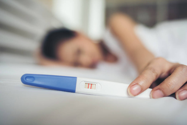 Triste femme se plaignant tenant un test de grossesse assis sur le lit - Photo, image