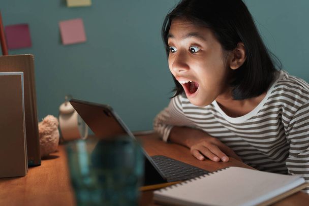 Menina asiática expressão animado no rosto enquanto assiste tablet, Ásia criança emoção surpresa no computador na mesa em casa à noite
 - Foto, Imagem