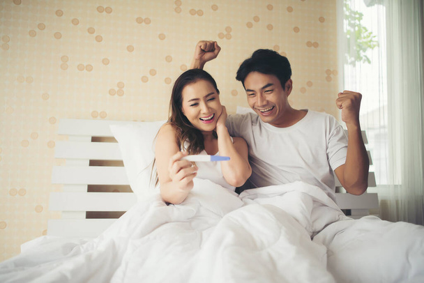 Ευτυχισμένο ζευγάρι χαμογελά μετά μάθετε θετικά τεστ εγκυμοσύνης στην κρεβατοκάμαρα  - Φωτογραφία, εικόνα