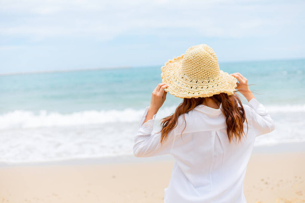 young woman wearin straw hat and walking on the beach. - Foto, afbeelding