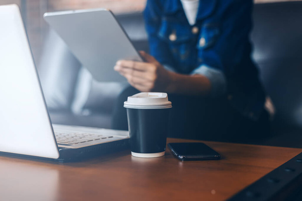 Eine Tasse Kaffee auf dem Tisch in der Nähe von Laptop und Frau verwenden Taplet Hintergrund. - Foto, Bild