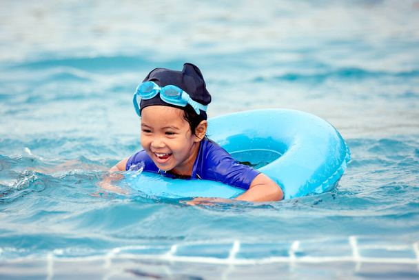 Süß asiatisch klein mädchen mit schwimmen ring ist having spaß bis schwimmen im pool - Foto, Bild
