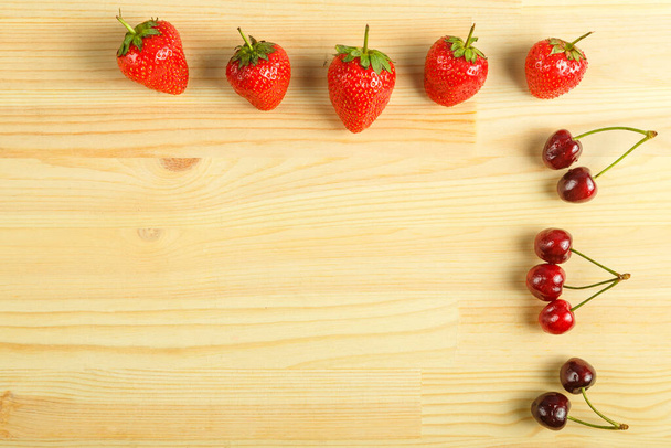Cherry and strawberry berries scattered on a wooden table. - Photo, Image