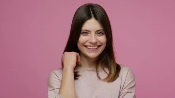 Lovely coquettish brunette woman touching hair and winking playfully, flirting and blinking eye as having some interesting idea, cheering up with happy look. studio shot isolated on pink background - Video