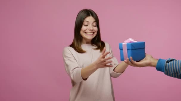 Happy birthday! Charming young woman expressing great joy and surprise when receiving present, shaking gift box, listening with interest what's inside. indoor studio shot isolated on pink background - Materiał filmowy, wideo