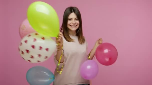 Cheerful happy energetic brunette woman laughing and dancing with colorful air balloons, enjoying birthday party, celebrating holiday, festive mood. indoor studio shot isolated on pink background - Filmagem, Vídeo