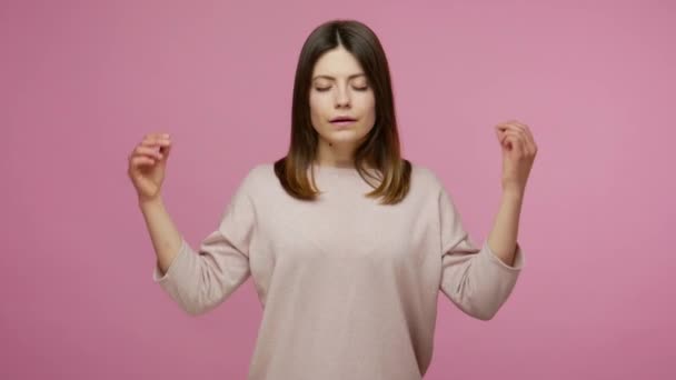 Meditation, peaceful mind. Calm brunette woman raising hands in mudra gesture and closing her eyes to relax, mental yoga practicing, concentration. indoor studio shot isolated on pink background - Кадры, видео