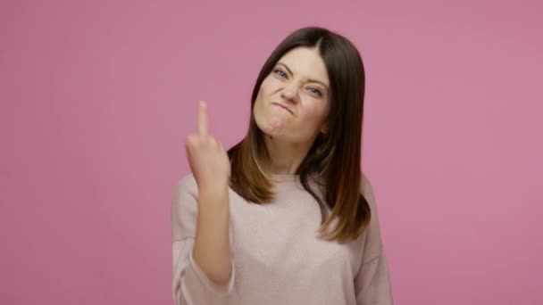 Rude vulgar brunette woman looking angry and showing middle finger, expressing protest and negativity to camera, rejecting with hate, aggressive emotions. studio shot isolated on pink background - Imágenes, Vídeo