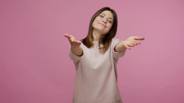 Please, all for you! Amiable kind brunette woman showing hand gesture Take everything for free, sharing love care and looking at camera with friendly smile. studio shot isolated on pink background - Filmati, video