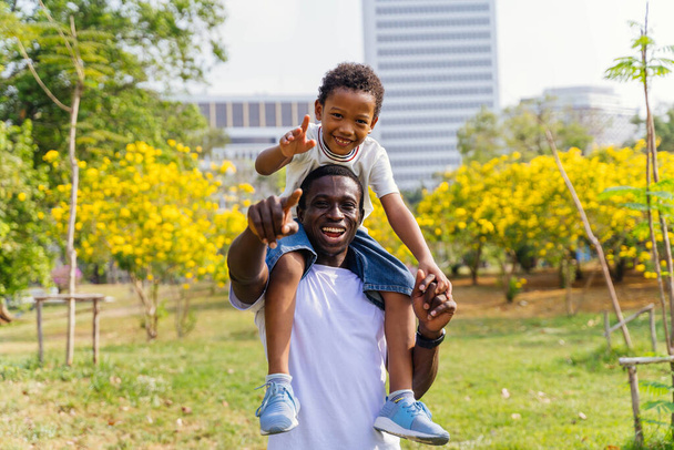 African American father and son piggyback in park. Fatherhood and happy family lifestyle concept - Фото, зображення