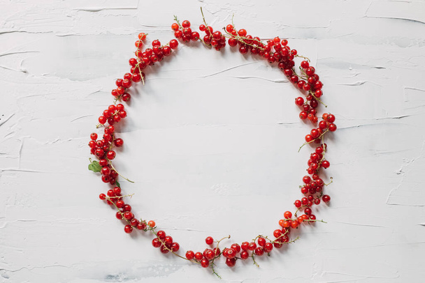 Round frame design from freshly picked redcurrant. Minimal flat lay composition with copy space from red berries on white. Healthy lifestyle. Support local farmers concept. Delicious organic summer fruits rich in vitamins.    - Photo, Image