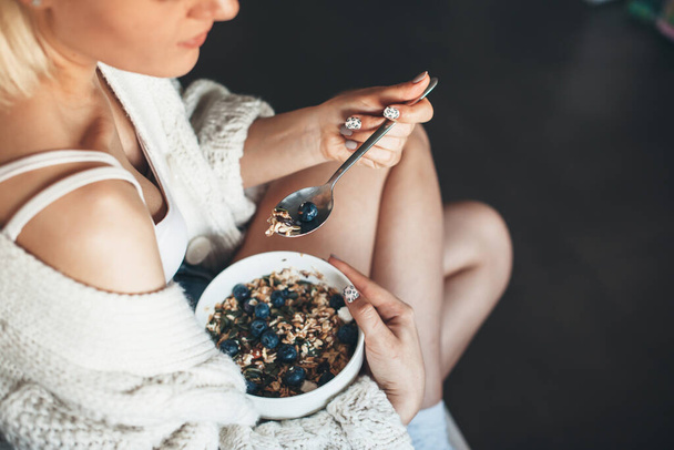 Foto vista superior de uma senhora loira em camisola de malha com hábitos saudáveis comer cereais sentados no chão
 - Foto, Imagem