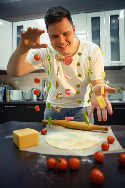 Człowiek produkujący pizzę, jak grzyby salami, ser z oliwek zamarza w powietrzu. domowe gotowanie - Zdjęcie, obraz