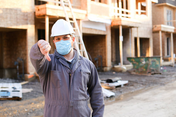 Foreman wearing mask and hardhat at construction site showing thumbs down. - Photo, Image